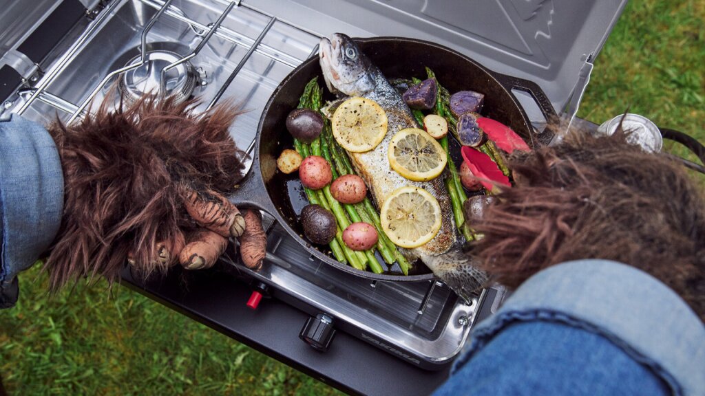 A close-up of a sasquatch cooking a freshly caught trout.