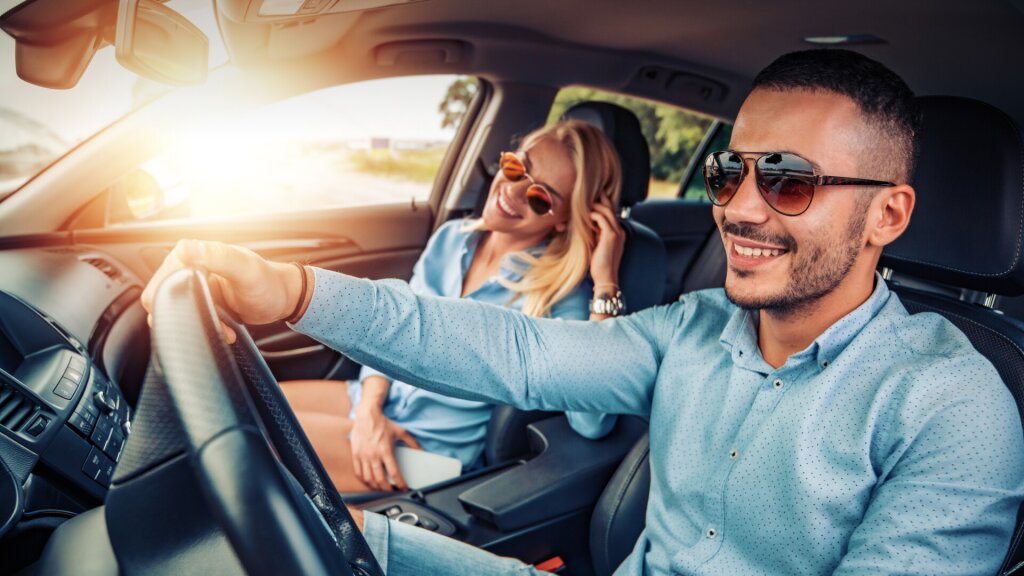 Photo of two people driving in a car while smiling.