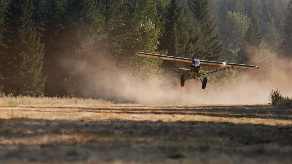 A photo of a low-flying bush plane over a dry field.