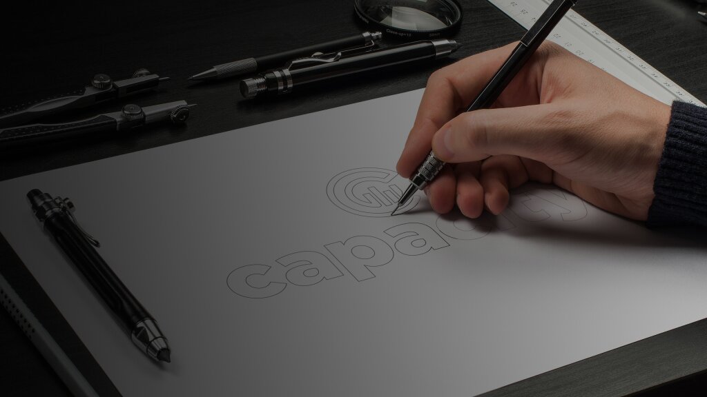 An image of a hand in the process of drawing a logo with a pencil.