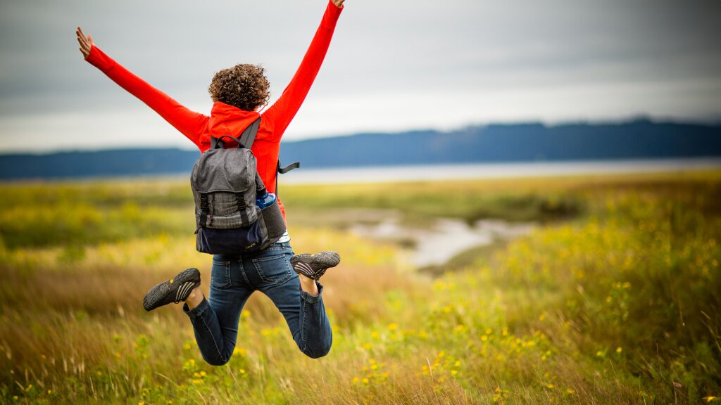 A young woman leaping into the area in a field of tall grass on the shores of the Hood Canal.
