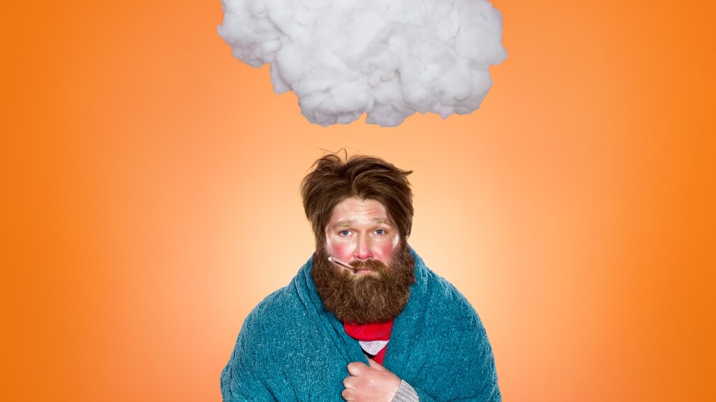 A bright, staged photo of a bearded man with a thermometer in his mouth with a fake cloud hovering above his head.