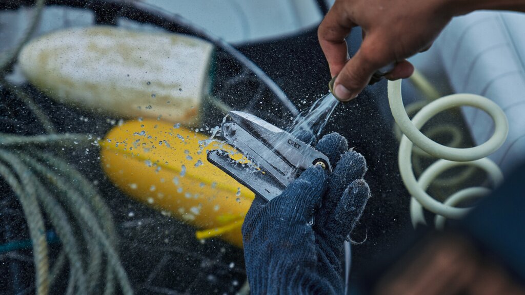 A CRKT field strip knife being cleaned with water from a hose.