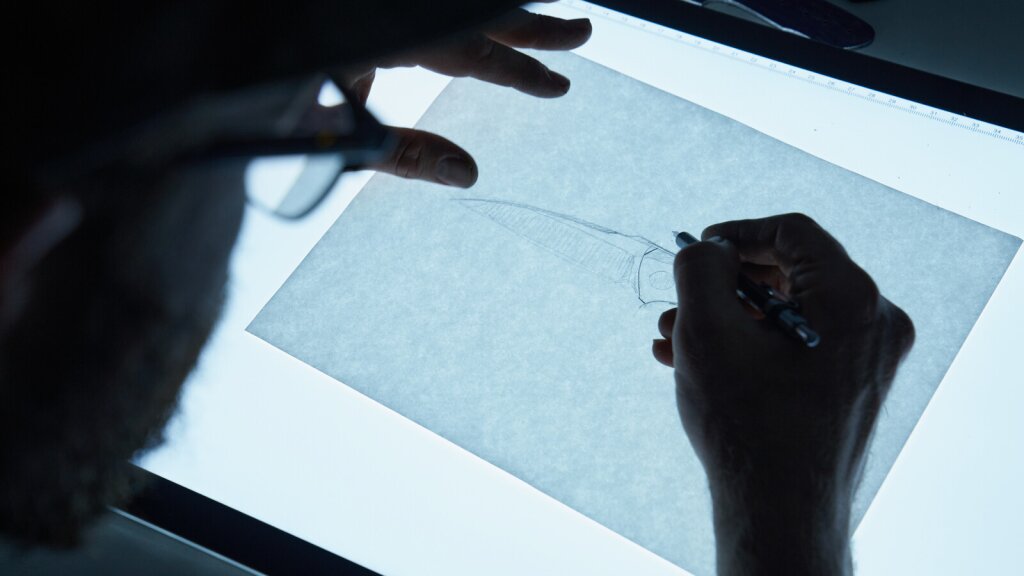 Lucas Burnley sketching a design for a knife on a lightbox.