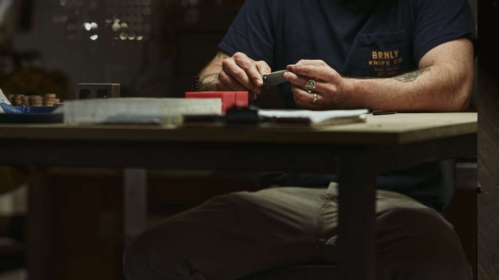 Lucas Burnley seated at a desk while inspecting a pocket knife.