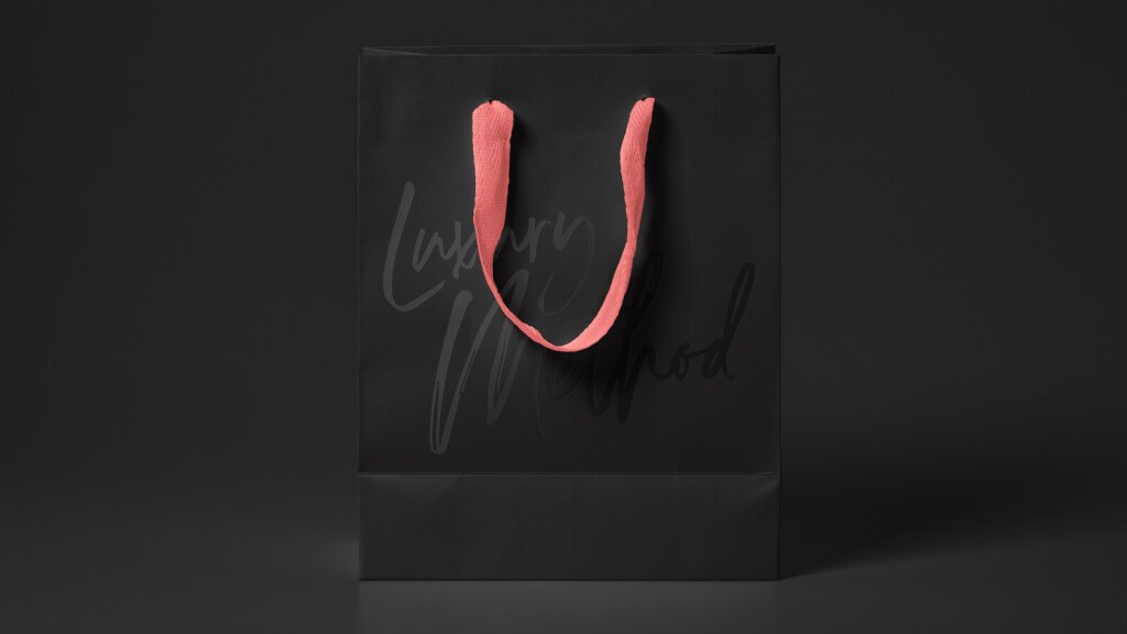A mock-up of a black bag with a spot varnished Luxury Method logo on it with a pink fabric handle.