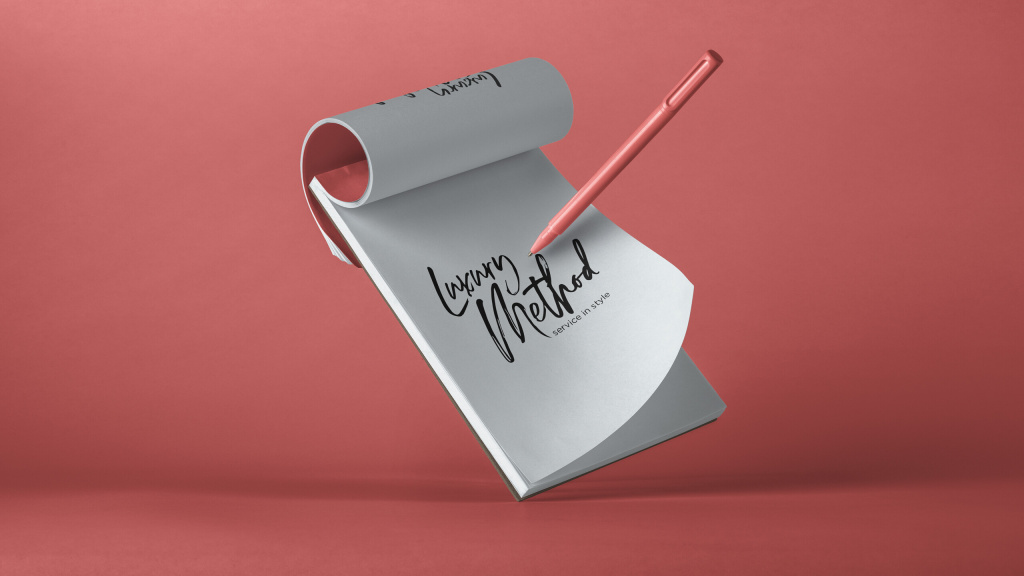A notepad with the Luxury Method logo written on a page with a bright pink background.