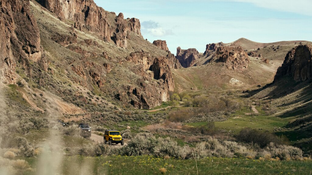 An image of off-road vehicles driving on a dirt road through a canyon.