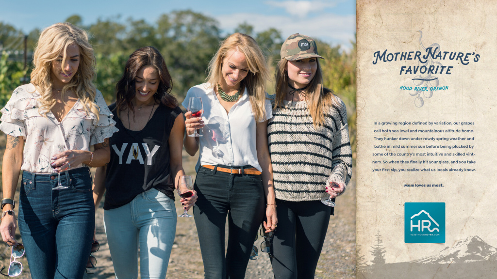A print ad for Visit Hood River featuring a group of friends walking in a vineyard while enjoying glasses of wine.