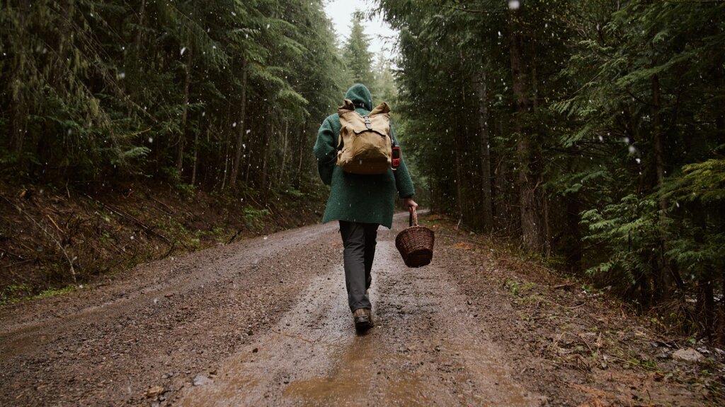 A photo of Yellow Elenor walking up a muddy, forest road while snow falls.