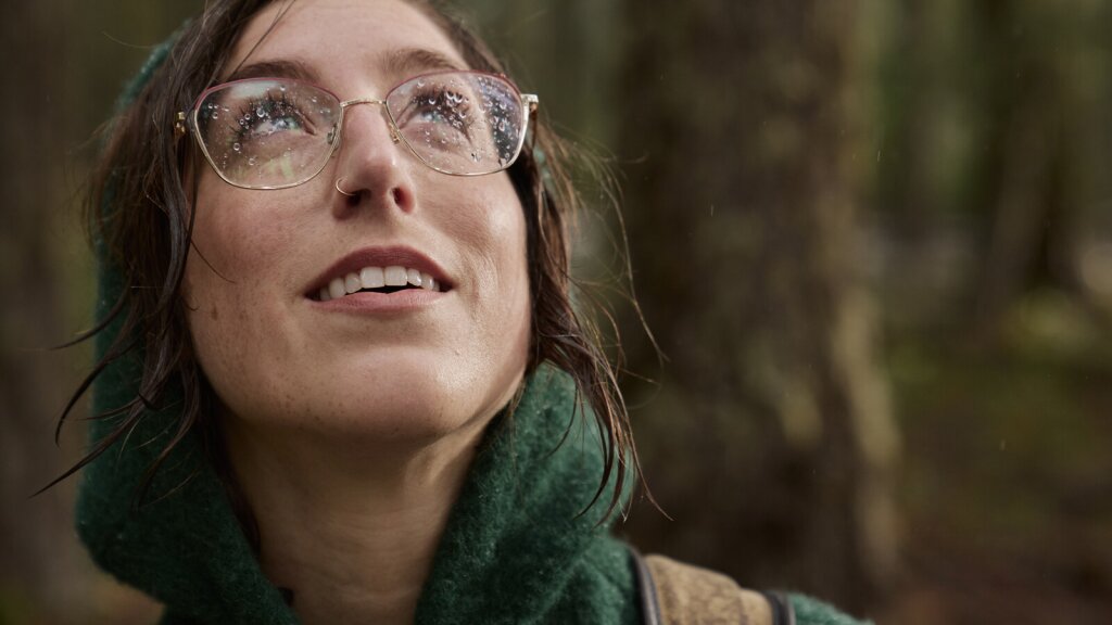 A close-up photo of Yellow Elanor's face with rain on her glasses as she looks skyward.