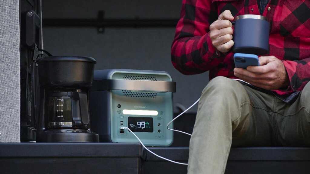 A photo of a man sitting in the door of his van while he makes coffee using his Yoshino portable battery.